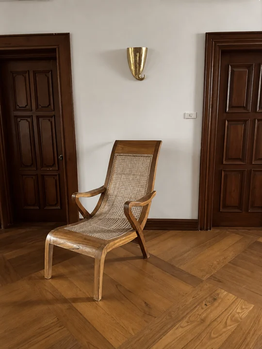 A handmade hardwood lounge chair with a woven cane seat between panelled timber doors
